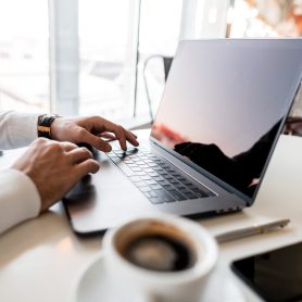 Professional successful business man sits in a bright office in a working day and works at a laptop. Young freelancer took a coffee break. Creative workplace.
